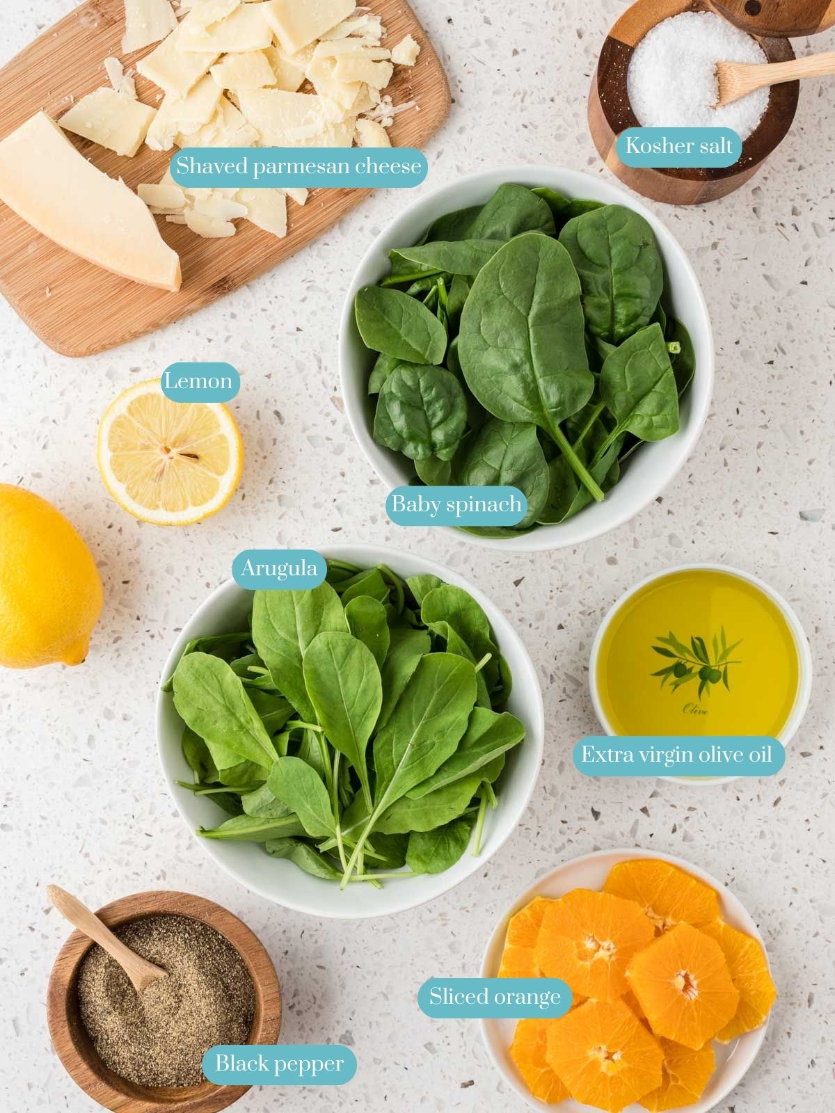 Overhead view of the ingredients in Arugula and Spinach Salad which include fresh arugula, fresh baby spinach, shaved Parmesan cheese, fresh lemon juice, extra virgin olive oil, Kosher salt, ground black pepper, and
sliced oranges. 
