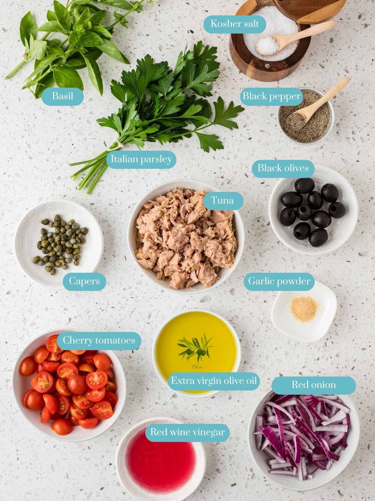 Overhead view of ingredients for Italian Tuna Salad. Ingredients include, tuna, basil leaves, Italian parsley, kosher salt, black pepper, capers, black olives, garlic powder, red onions, cherry tomatoes, and red wine vinegar.