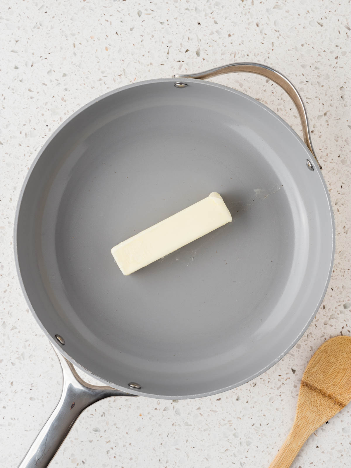 One stick of butter in a pan with a wooden spoon set to the side. 