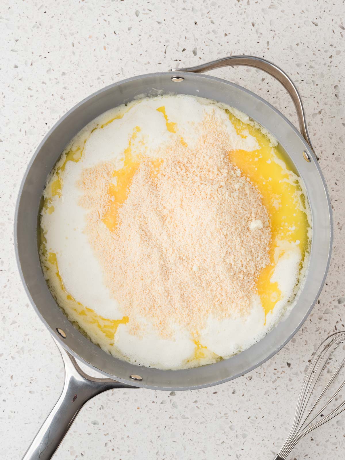 Parmesan cheese and heavy cream added to the butter garlic mixture in a pan with a whisk set to the side.