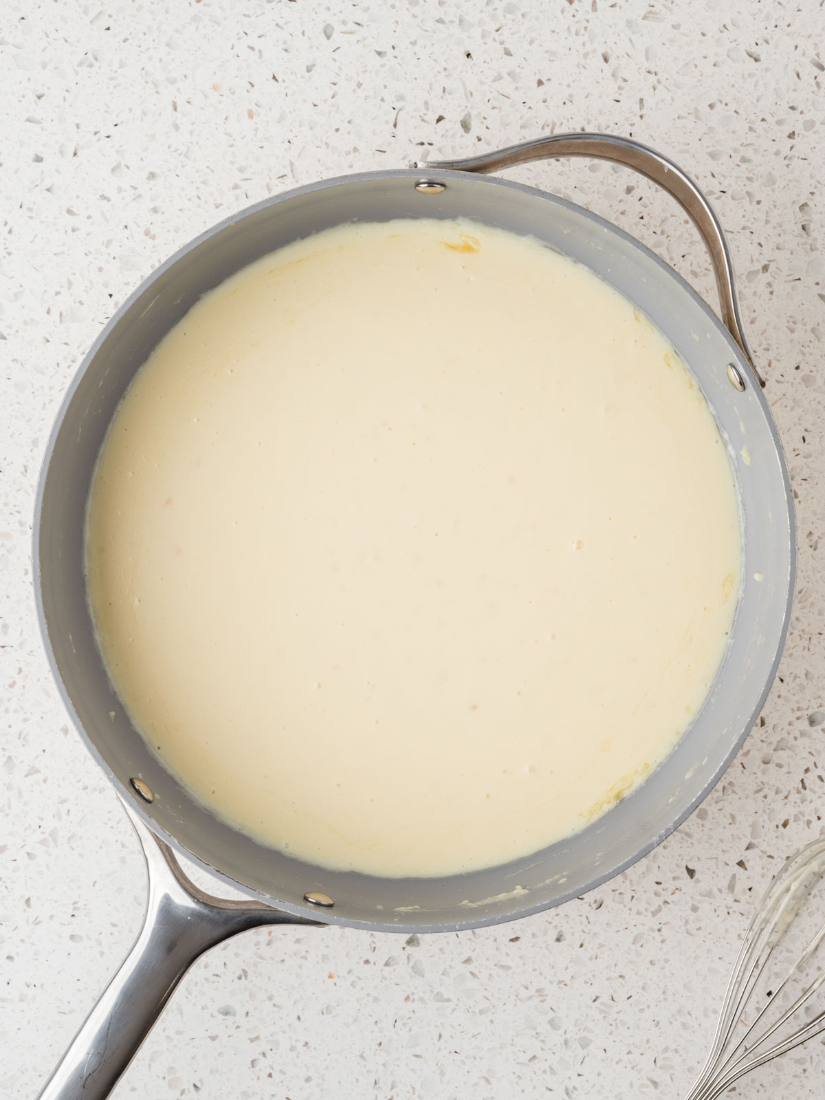 Alfredo sauce in the pan with a whisk set to the side.