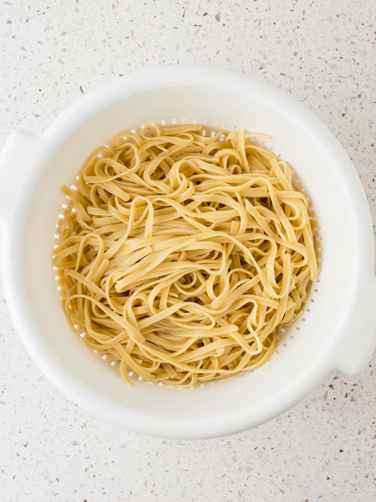 Cooked fettuccine noodles in a colander.