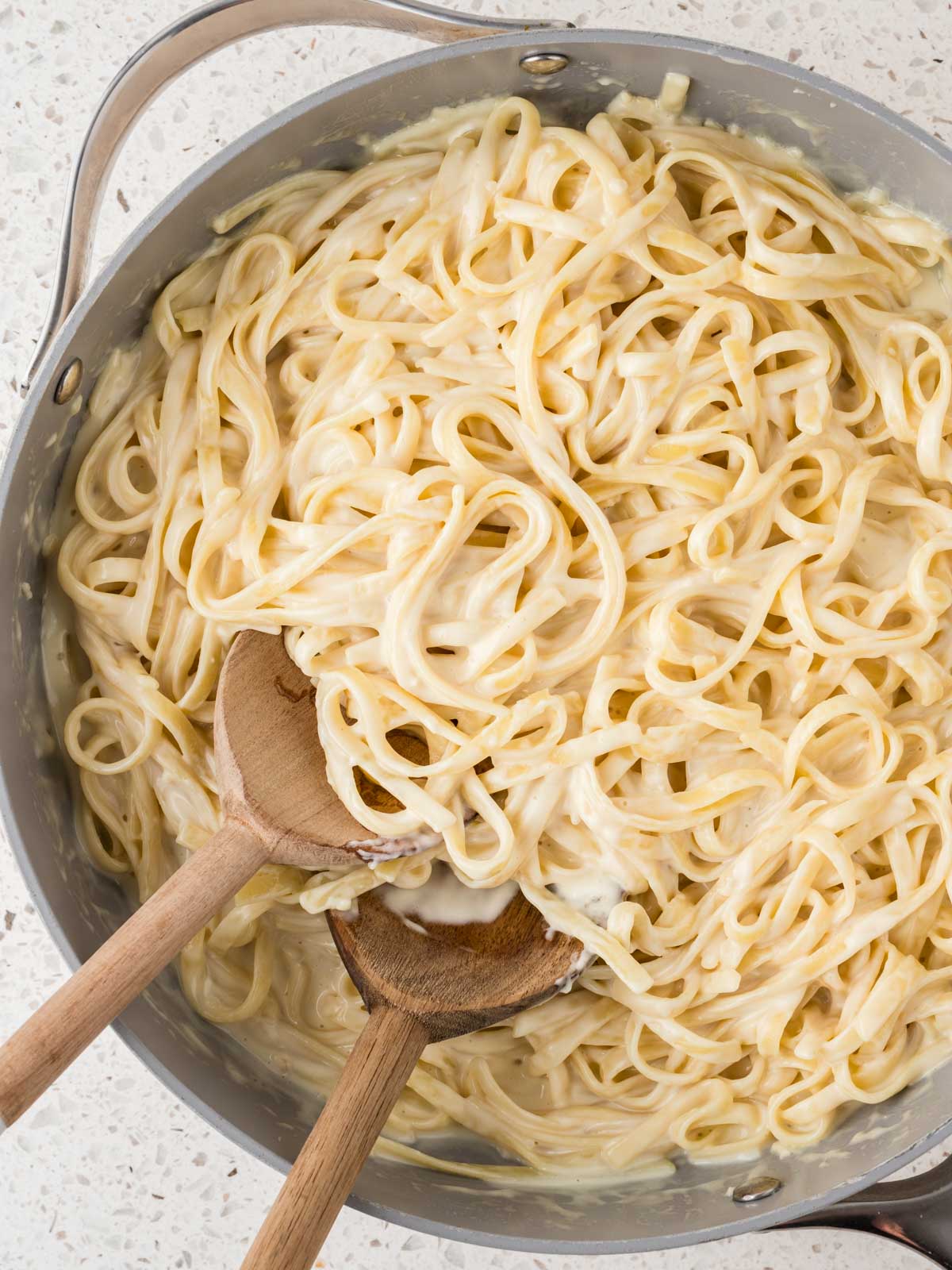 Homemade Fettucine Alfredo in a pan with two wooden spoons.