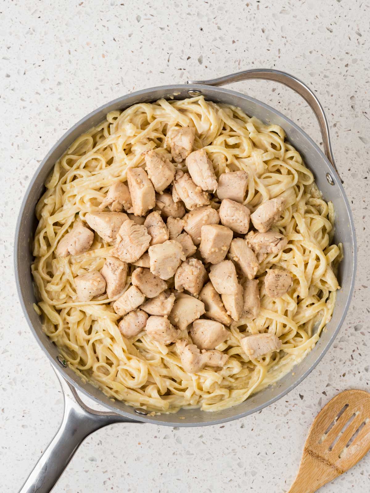 Cooked chicken breast cut into cubes and in the pan with the fettuccine noodles and sauce. 