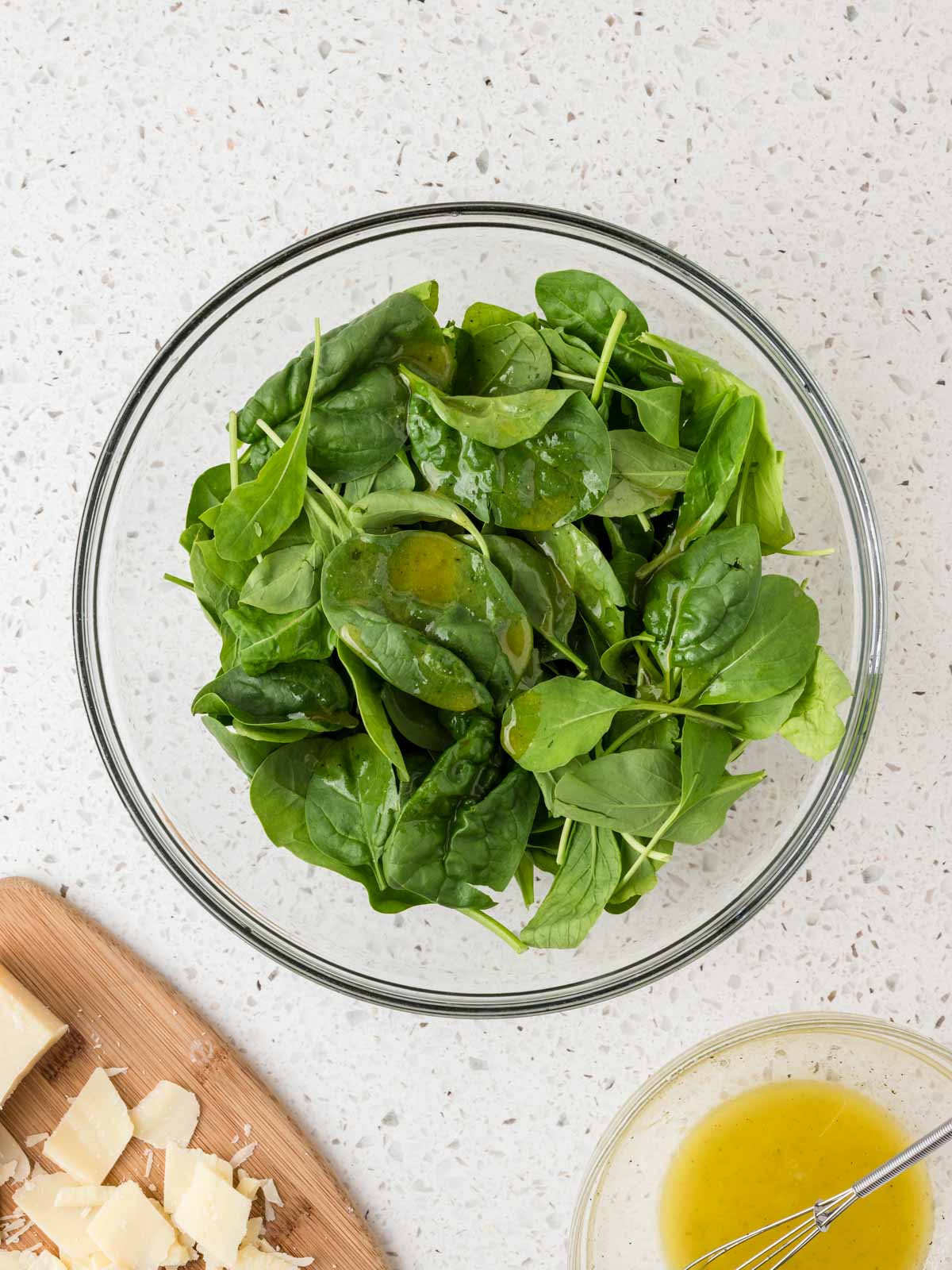 Dressing drizzled over the arugula and spinach mixture in the glass bowl. 
