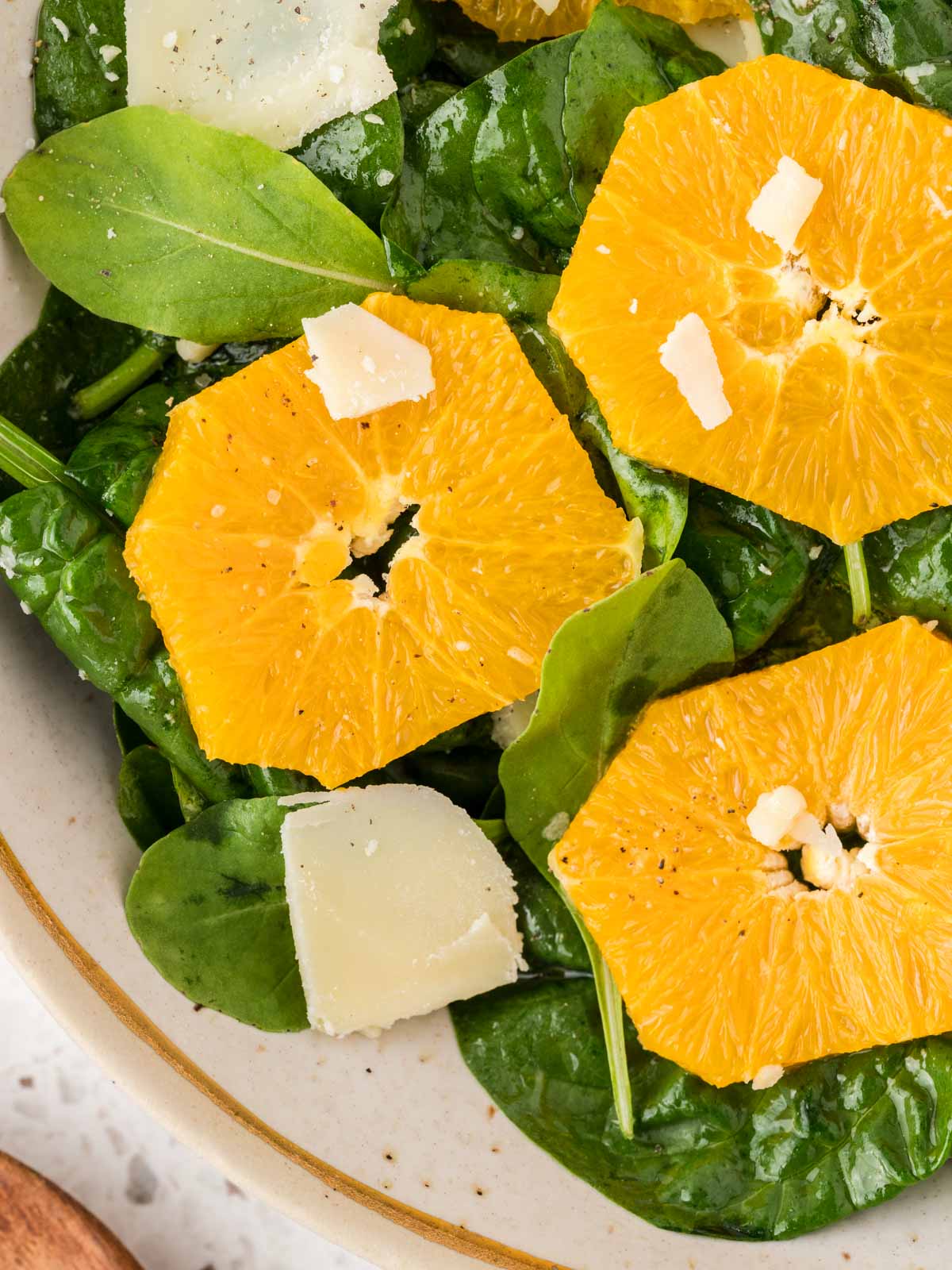 Arugula and spinach salad in a serving bowl. The salad is garnished with sliced oranges and shaved parmesan cheese. 