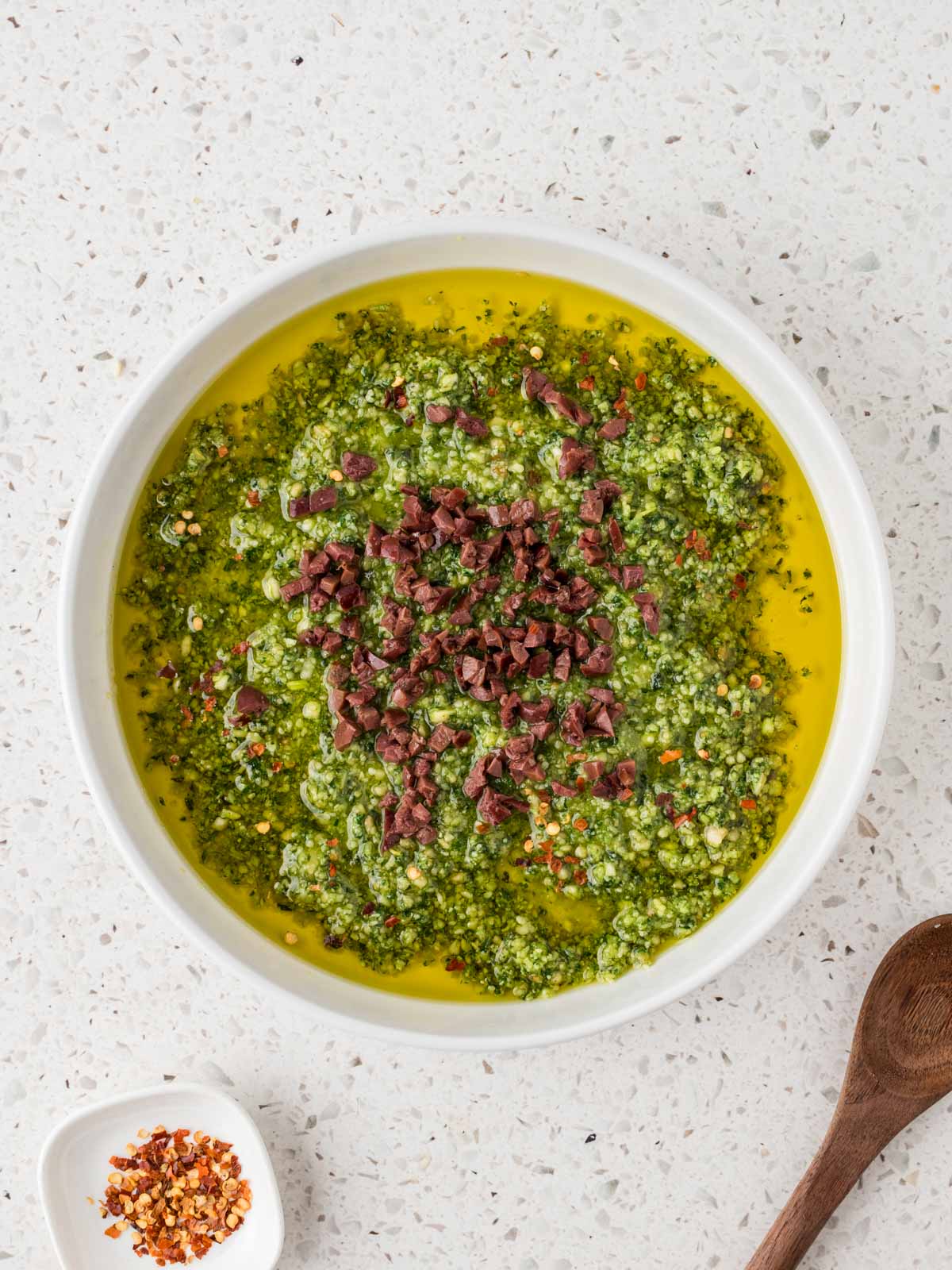 Olive oil with the pesto mixture and 6 finely chopped Kalamata olives in a small bowl.