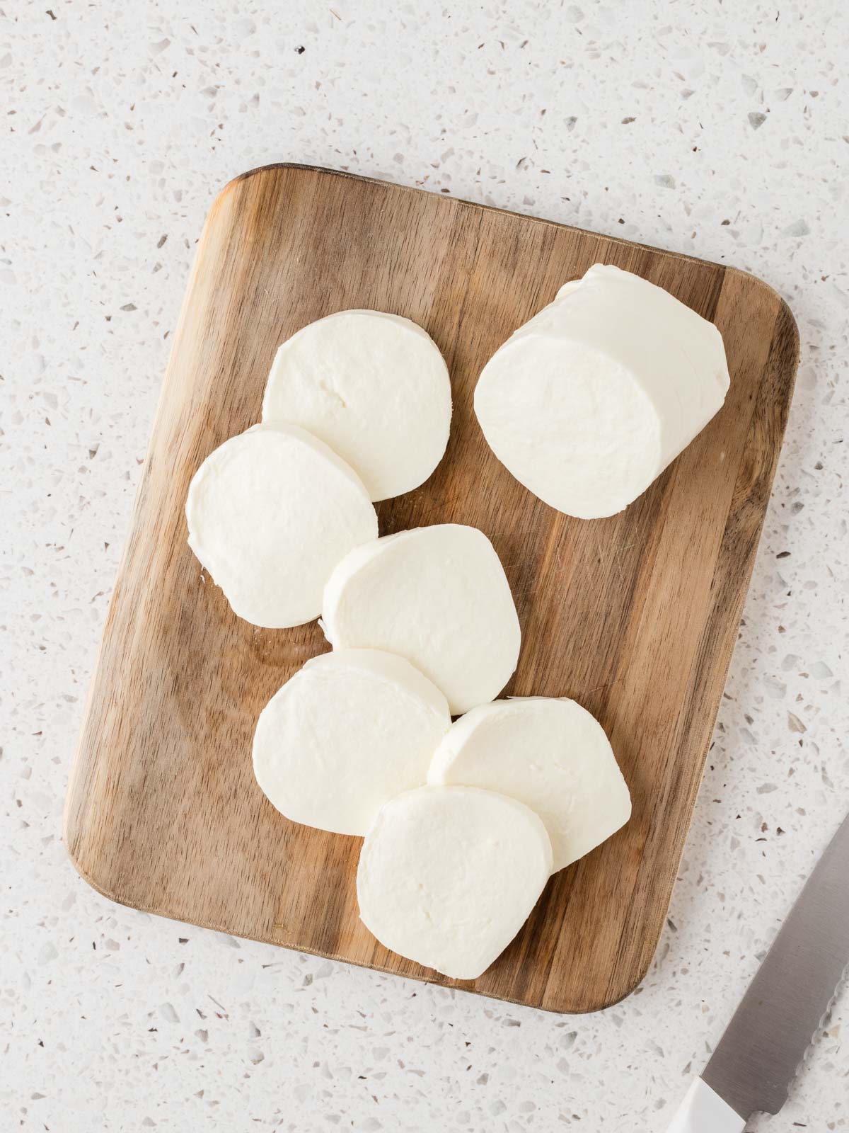 Fresh mozzarella sliced on a cutting board with a knife to the side. 