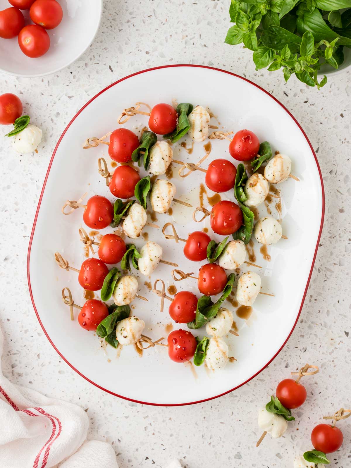 Caprese salad skewers on a platter surrounded by extra skewers and basil leaves. 