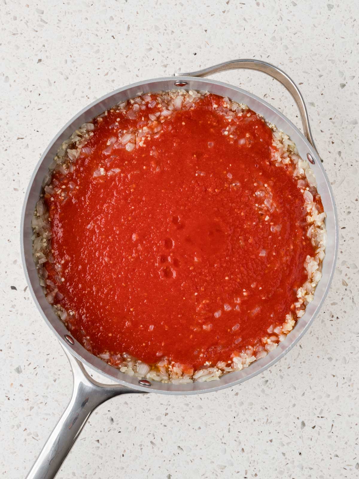 Sauteed onions with San Marzano tomatoes poured into the pan.