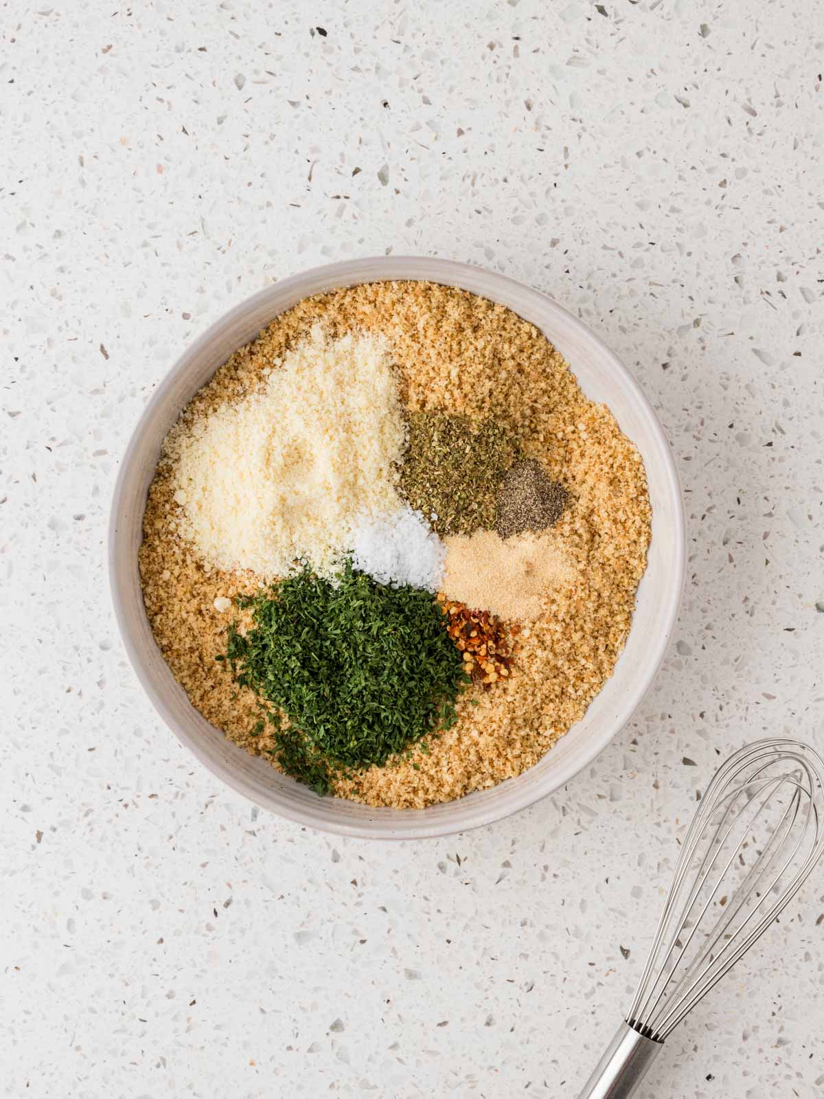 Toasted breadcrumbs in a bowl with parsley, oregano, garlic powder, Parmesan, red pepper, salt, and pepper. 