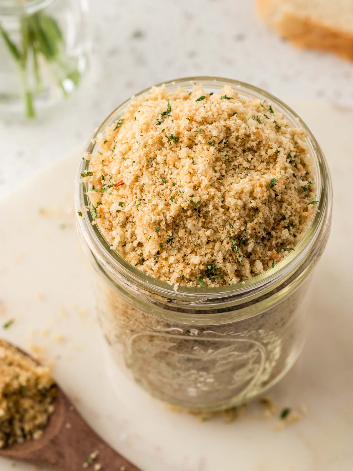 Homemade Italian Breadcrumbs in a jar with a spoonful of breadcrumbs on the counter. 