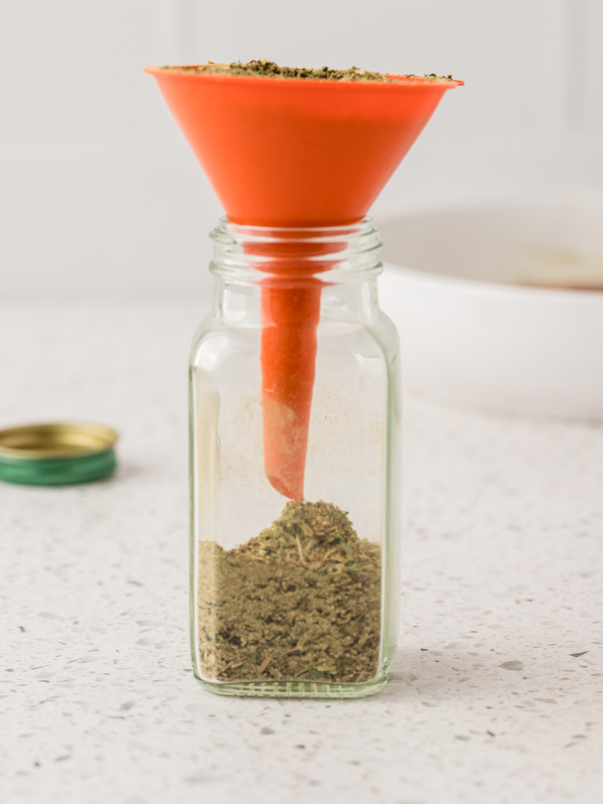 Homemade Italian seasoning being poured into a small glass jar with a funnel for storage. 