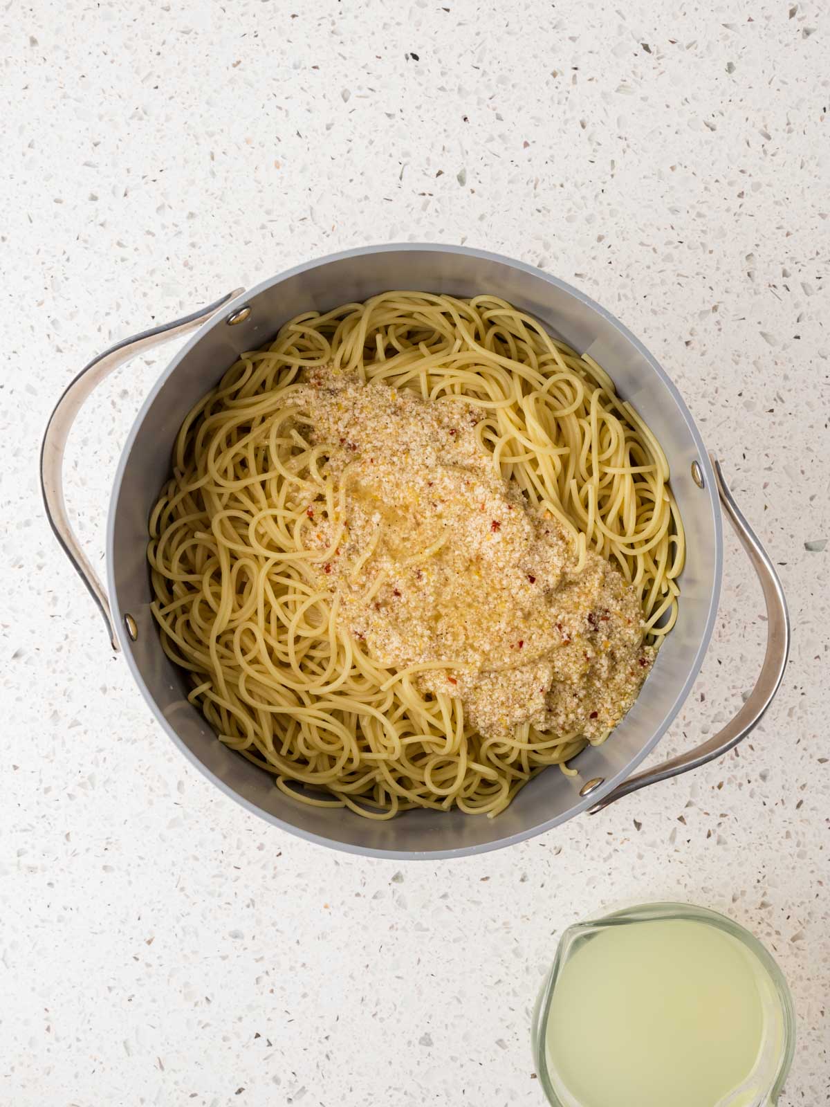 Pasta noodles in the pan with the lemon sauce poured over the top with pasta water on the side. 