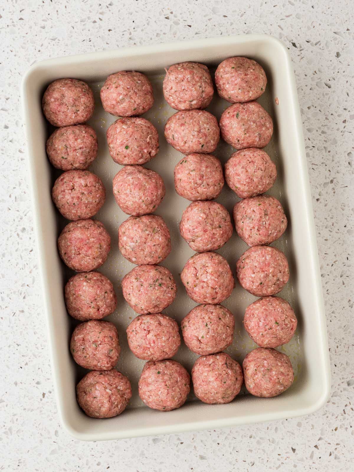 Rolled meatballs in a greased baking dish ready for the oven.
