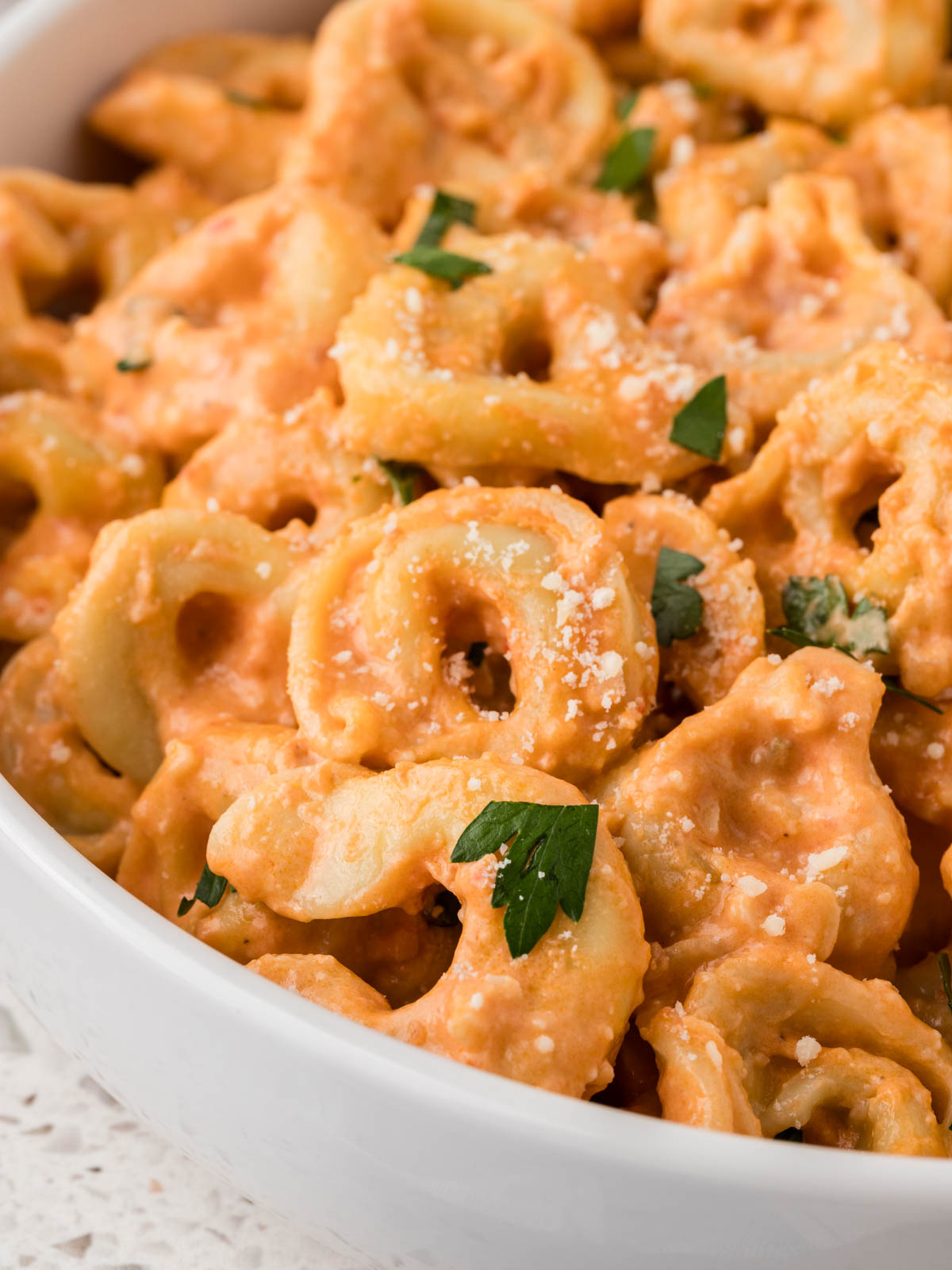Tortellini with rose sauce in a serving bowl garnished with parmesan and fresh chopped parsley.