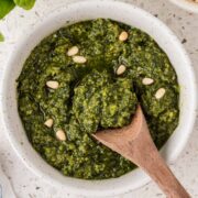 Basil pesto sauce in a small bowl garnished with pine nuts and a spoon in the bowl.