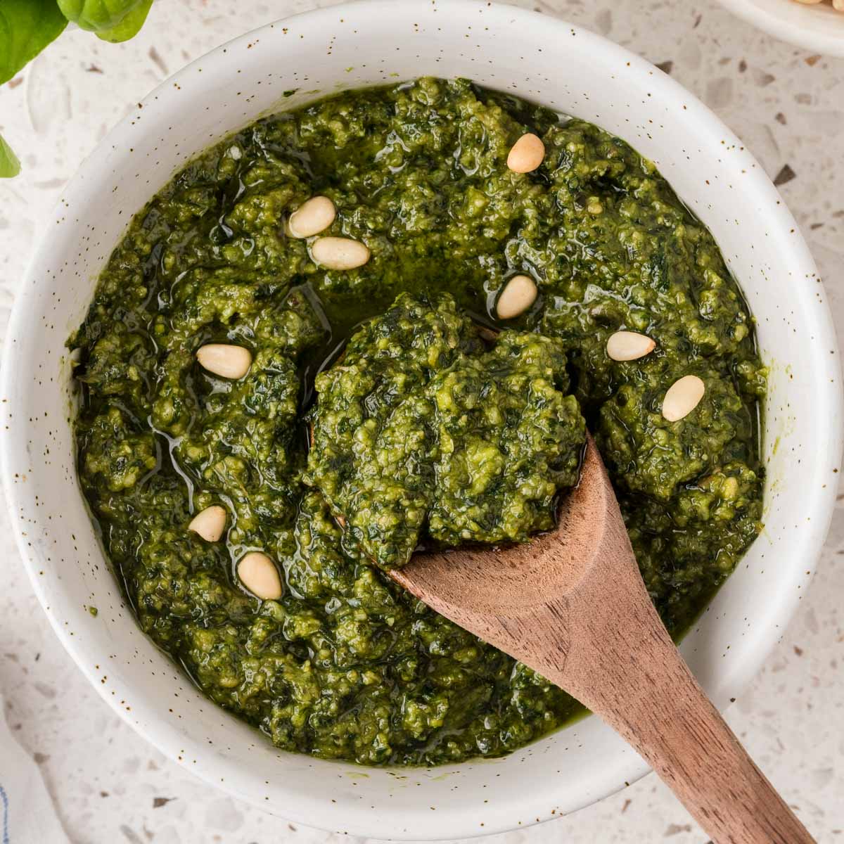 Basil pesto sauce in a small bowl garnished with pine nuts and a spoon in the bowl.