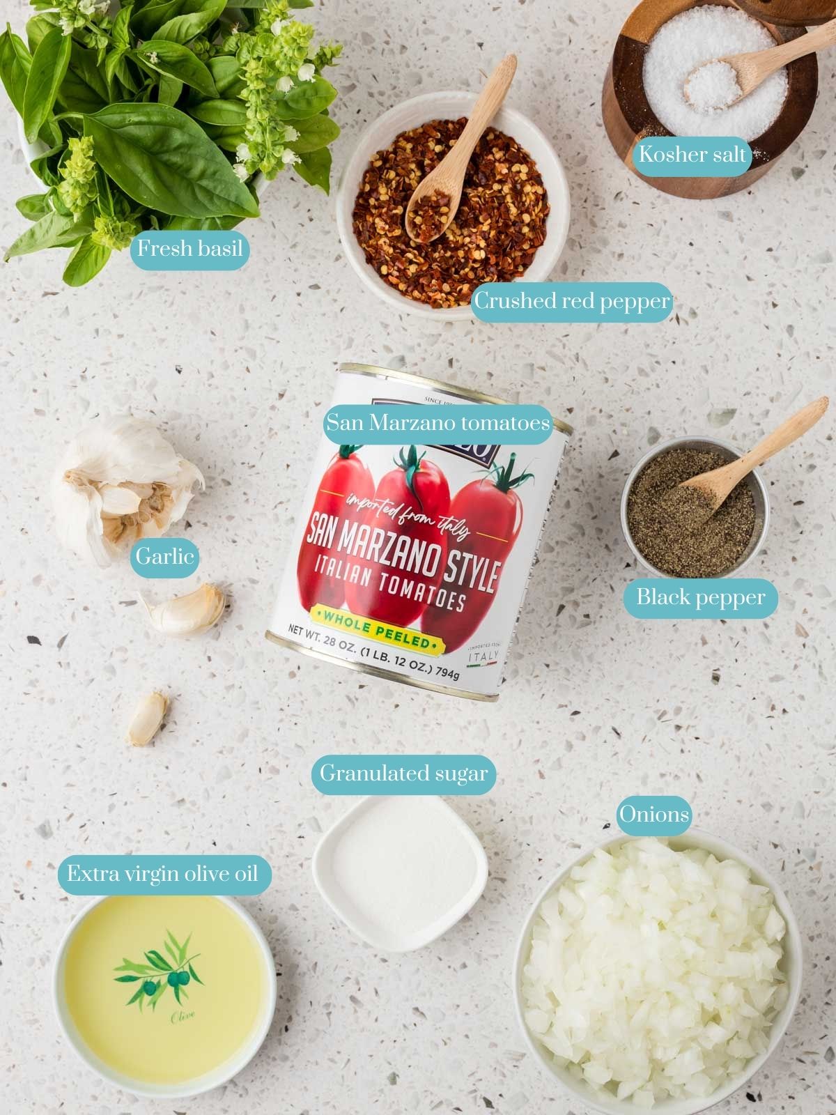 Overhead view of ingredients for Easy Marinara Sauce which include extra virgin olive oil, garlic, finely chopped onion, whole peeled San Marzano tomatoes, kosher salt, granulated sugar, ground black pepper, crushed red pepper flakes, and fresh basil leaves.