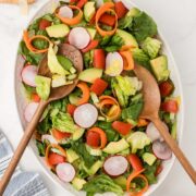 Salad with red wine vinaigrette on a white serving platter with wooden salad serving spoons.