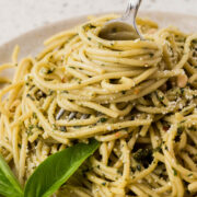 Basil pesto pasta on a plate with pasta twirled around a fork. The dish is garnished with fresh basil.