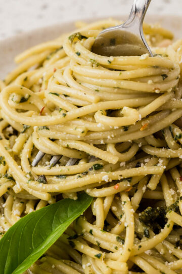 Basil pesto pasta on a plate with pasta twirled around a fork. The dish is garnished with fresh basil.