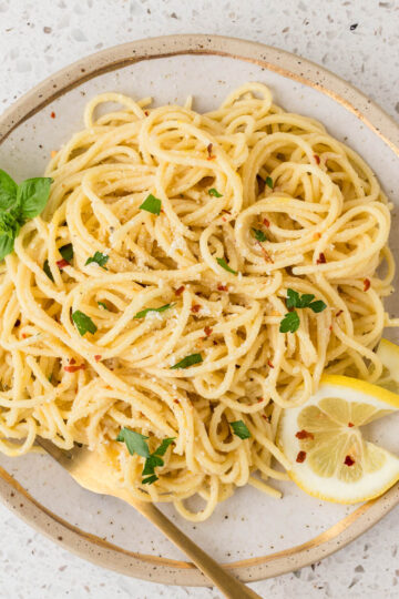 Lemon spaghetti on a gold rimmed plate garnished with fresh basil, crushed red pepper and a lemon slice.