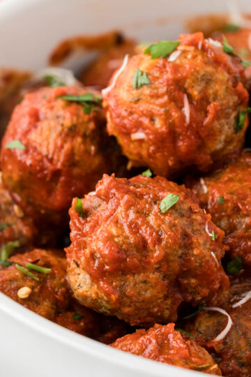 Homemade Italian Meatballs piled in a serving bowl, garnished with fresh chopped parsley.