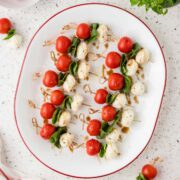 Caprese skewers arranged on a white platter with a red rim.