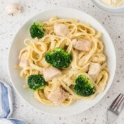 Chicken broccoli alfredo plated in the center, surrounded by a garlic clove, parmesan cheese and a fork.