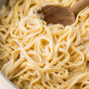 Homemade fettuccine alfredo prepared in a pan with a wooden spoon scooping the noodles.