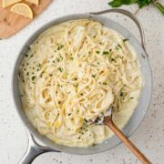 Lemon fettuccine alfredo in a pan with a wooden serving spoon.