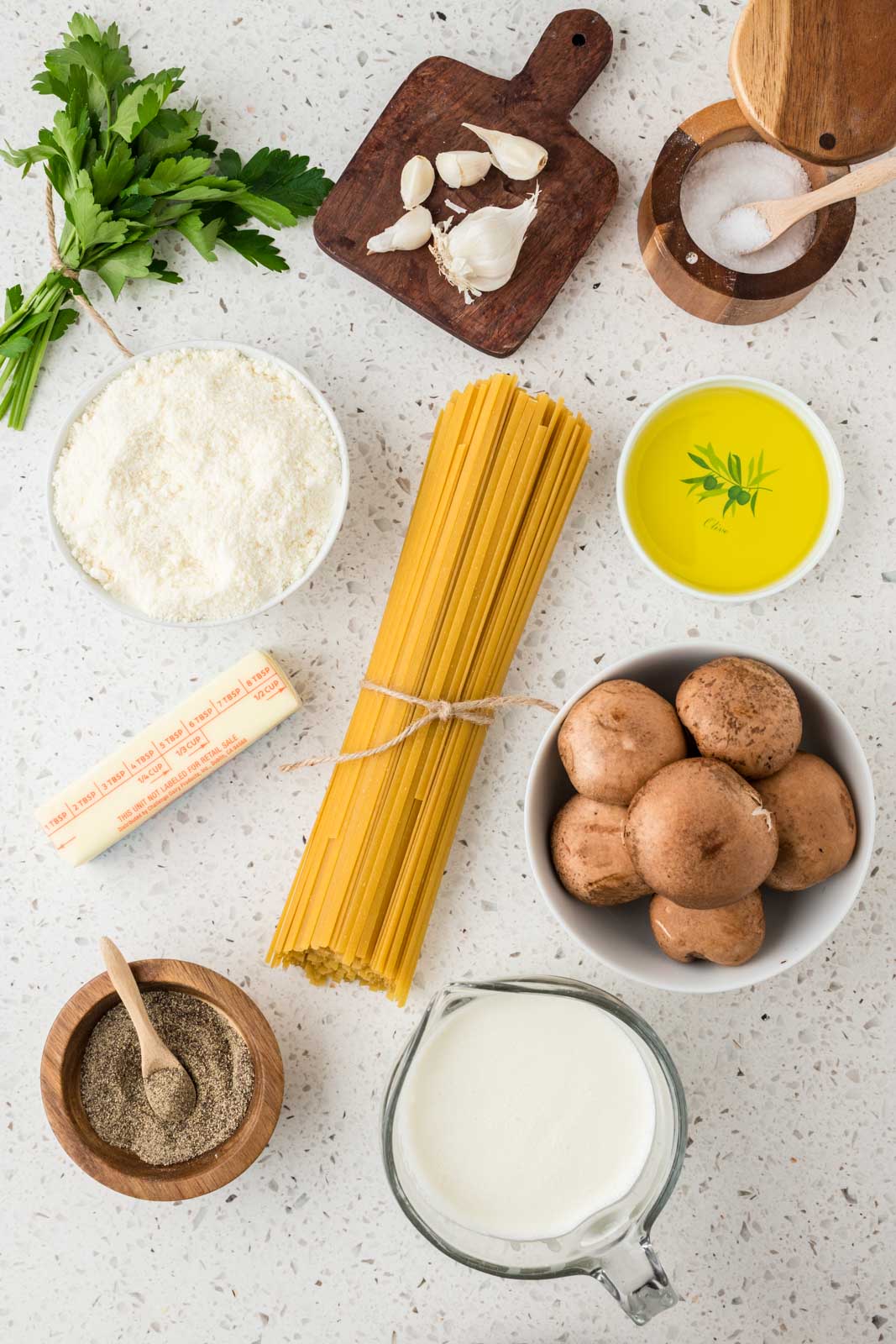 All ingredients for Creamy Mushroom Fettuccine Alfredo including Fettucine, Garlic, Kosher Salt, Parmesan Cheese, Butter, Pepper, Heavy Cream, Mushrooms, Olive Oil, Parsley. 