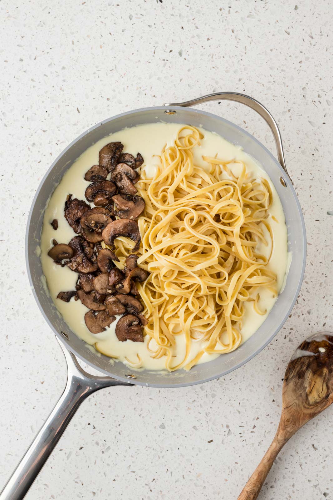 Fettuccine noodles and sauteed mushrooms are added to the alfredo sauce in the pan.