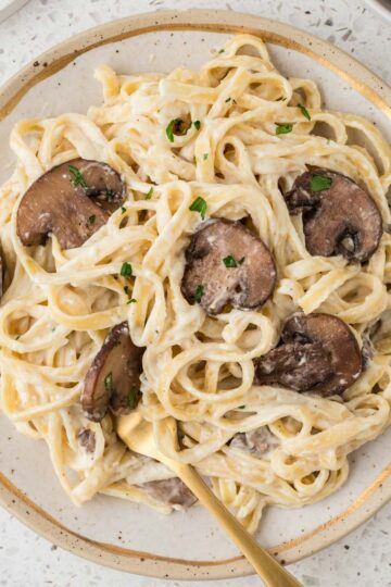 Creamy Mushroom Fettuccine Alfredo plated with a gold fork.