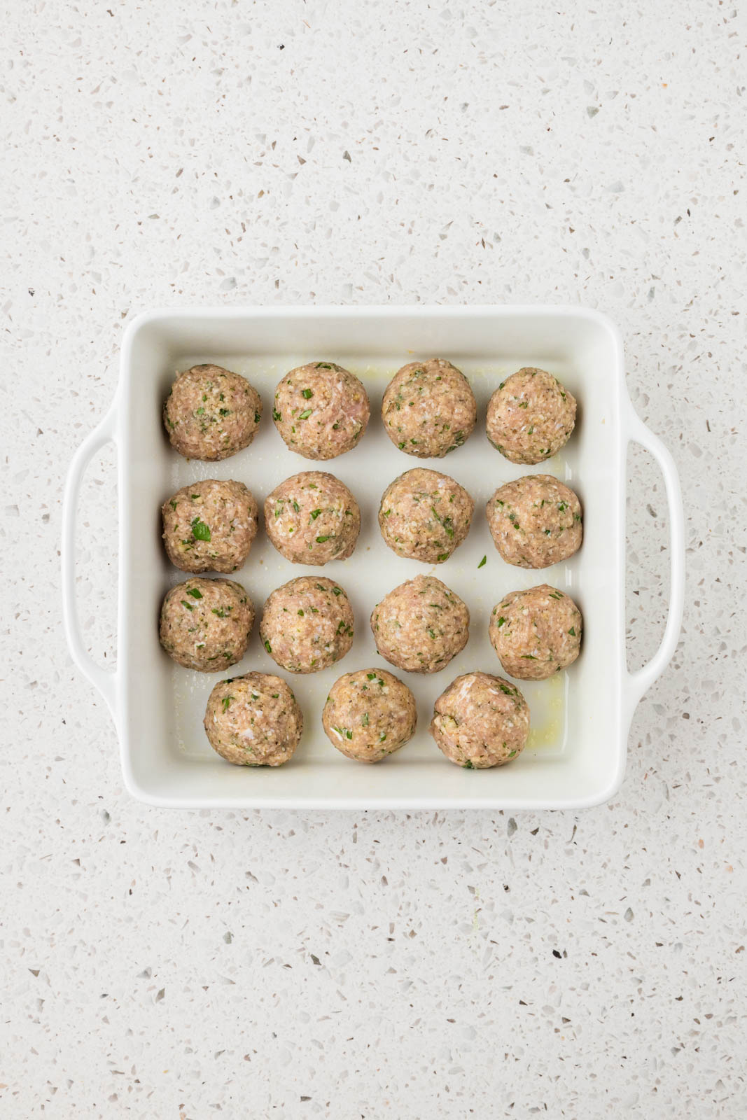 Raw chicken meatballs in a baking dish.