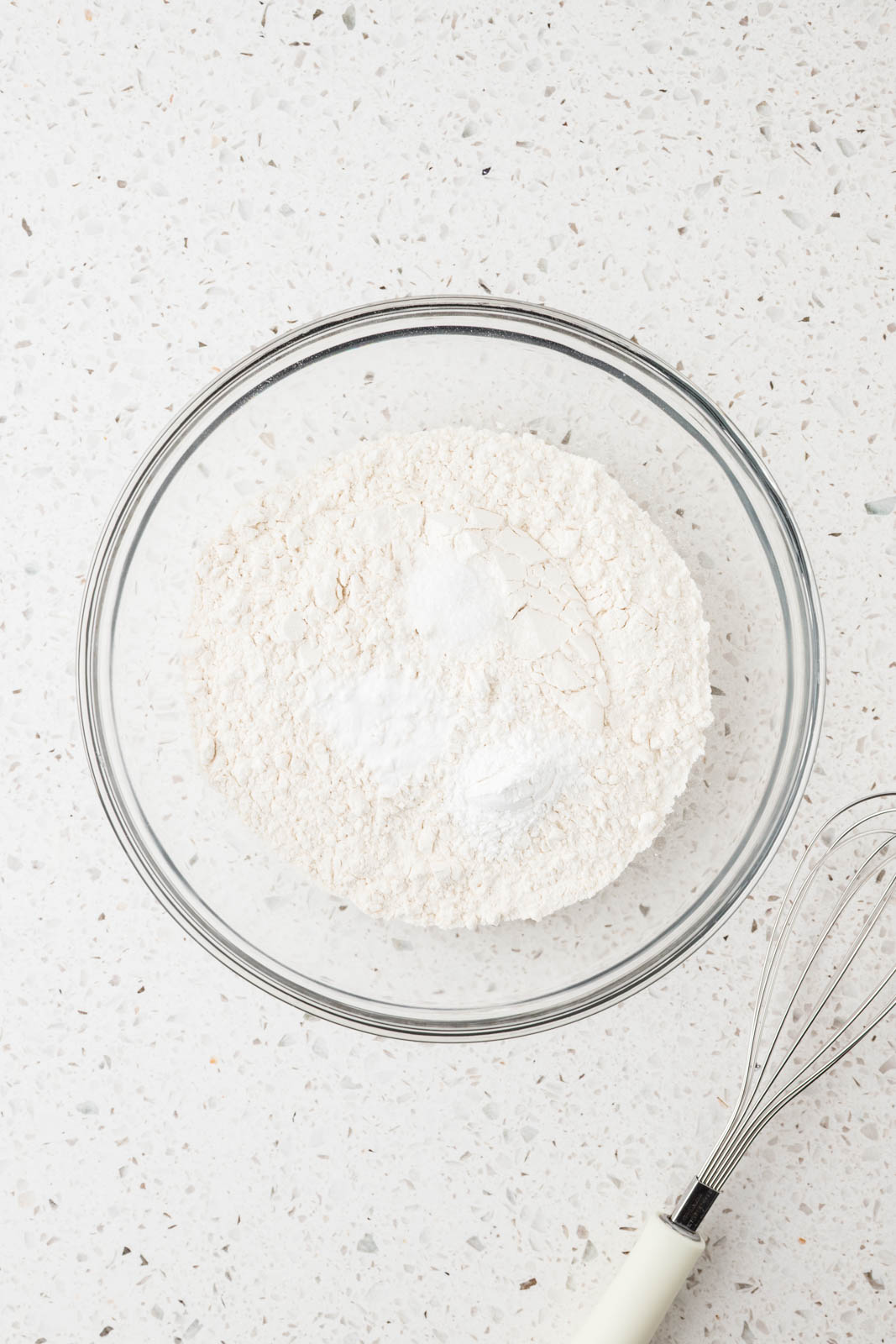 Flour, baking soda, baking powder, and kosher salt in a mixing bowl with a whisk along side.
