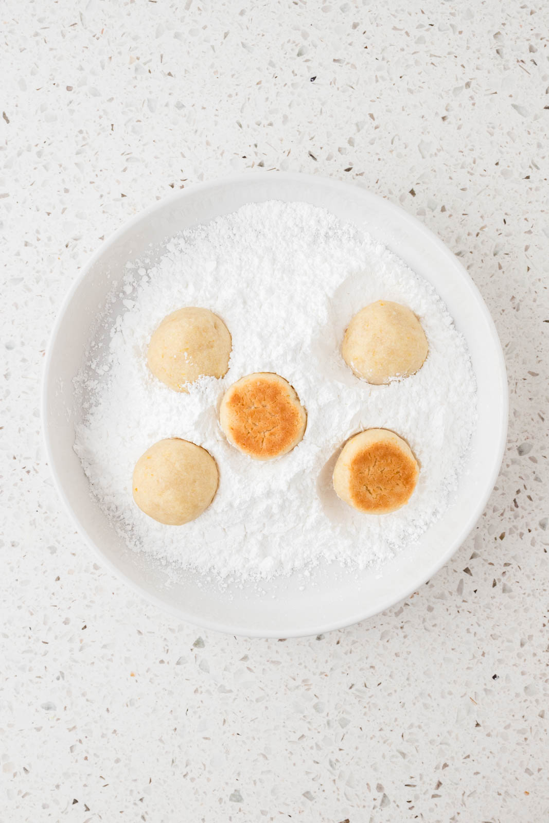 Cookies in a dish of powdered sugar.