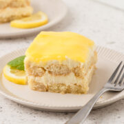 Piece of lemon tiramisu on a plate with a lemon garnish and a fork.