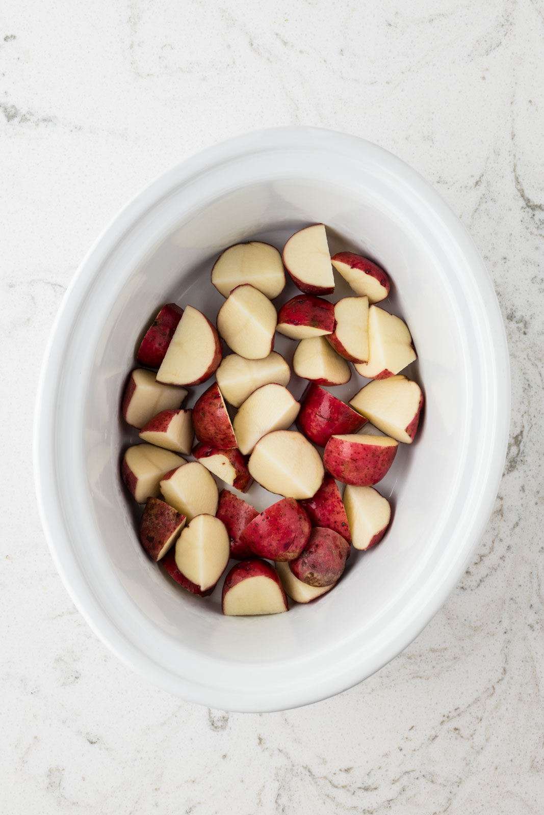 Quartered potatoes in the bottom of the slow cooker.