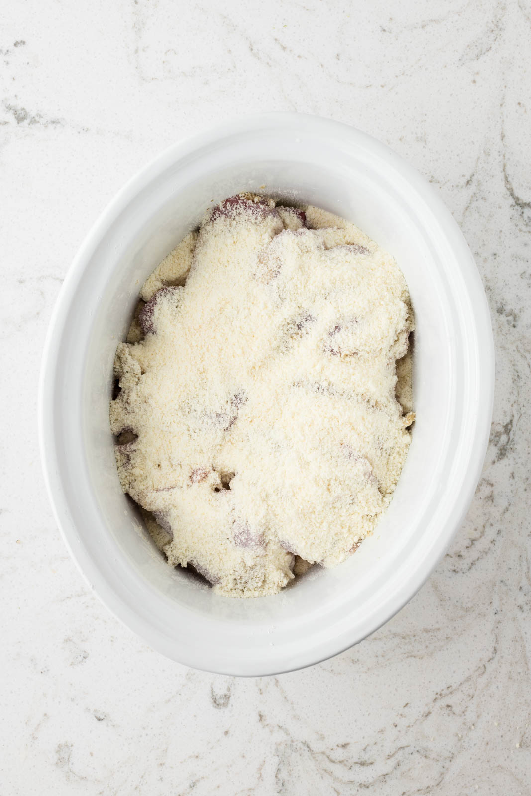 Chicken and potatoes in the slow cooker covered with parmesan cheese.