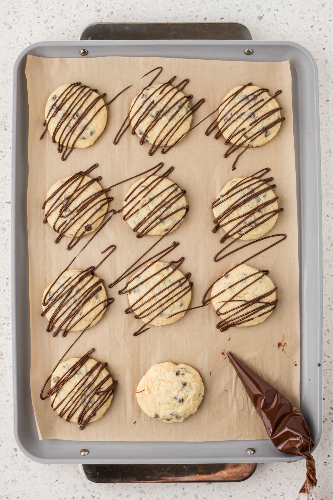 Cannoli cookies on a baking sheet drizzled with melted chocolate.