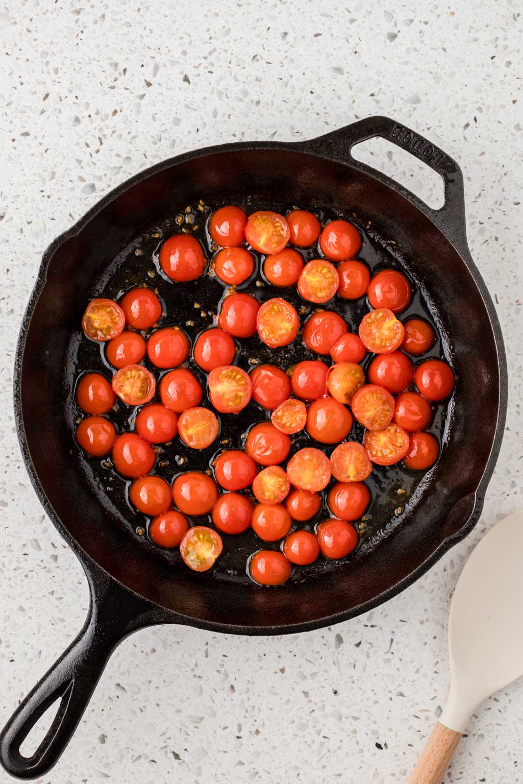 Halved cherry tomatoes with olive oil in a cast iron pan. 