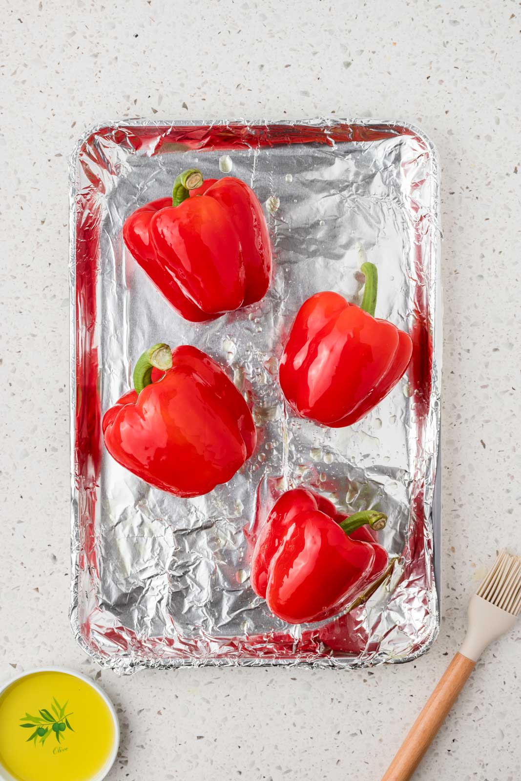 Red peppers basted with olive oil on a foil lined baking sheet.