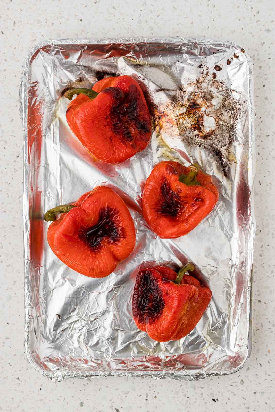 Roasted red peppers baked on a foil lined baking sheet.