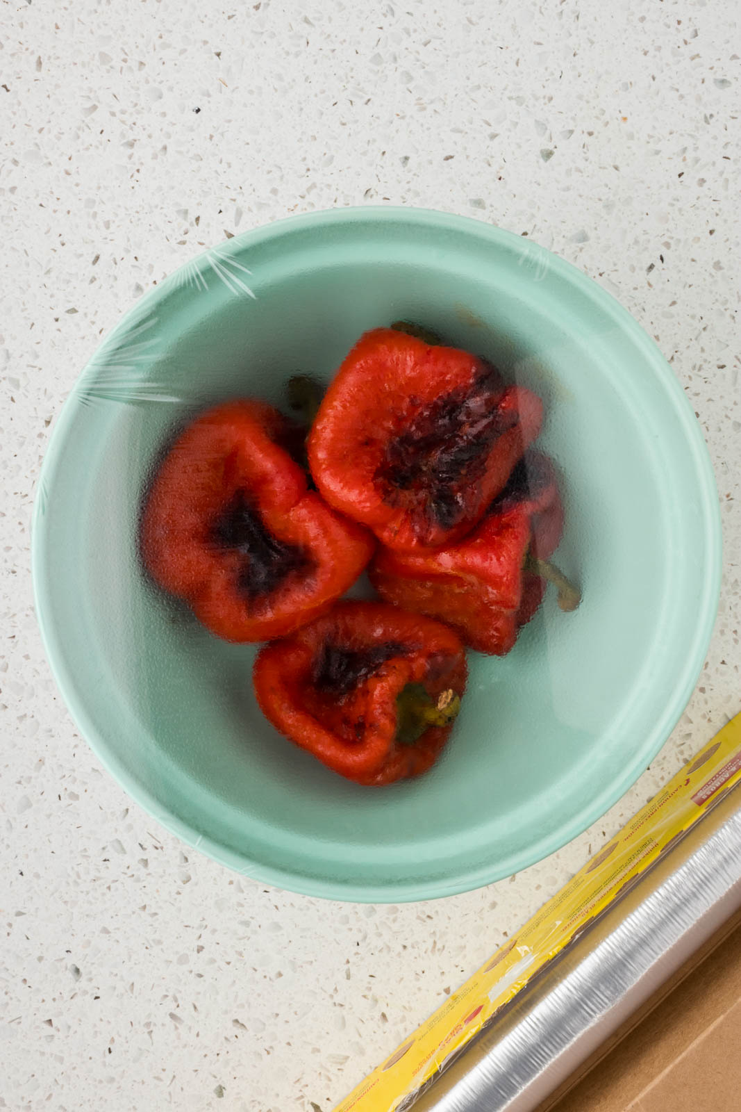 Roasted red peppers in a bowl covered with plastic wrap.