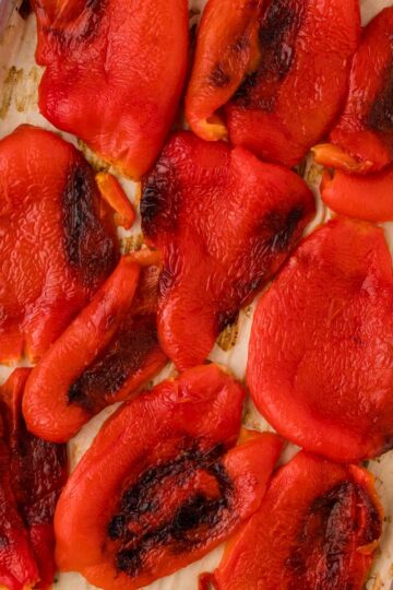 Roasted red peppers on a parchment-lined baking sheet.