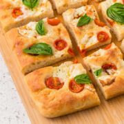 Caprese focaccia bread cut into pieces on a wooden board.
