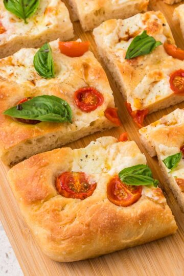 Caprese focaccia bread cut into pieces on a wooden board.