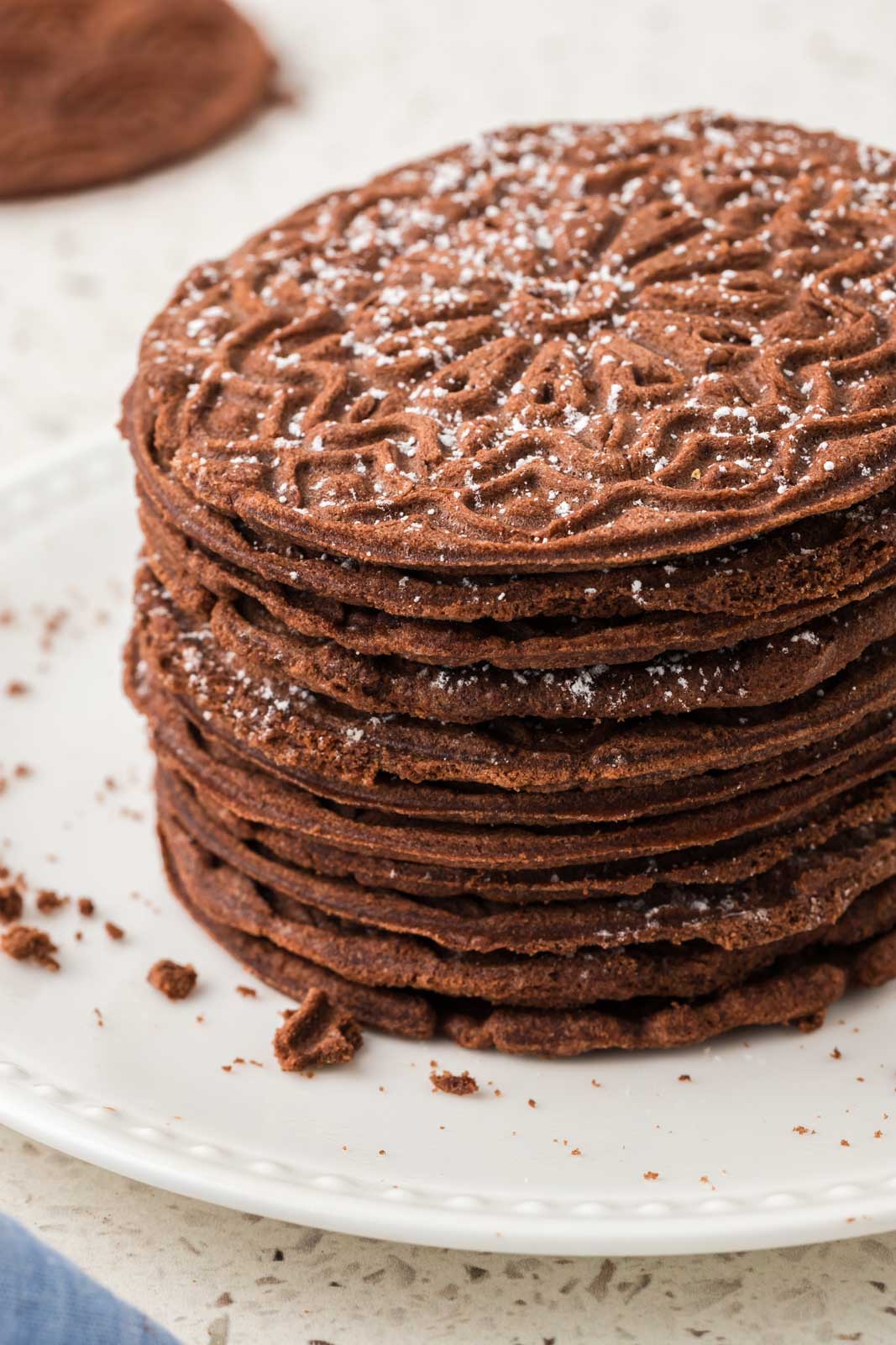 Chocolate pizzelles stacked on a plate.